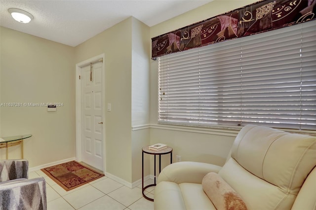 living area with light tile patterned flooring, a textured ceiling, and baseboards