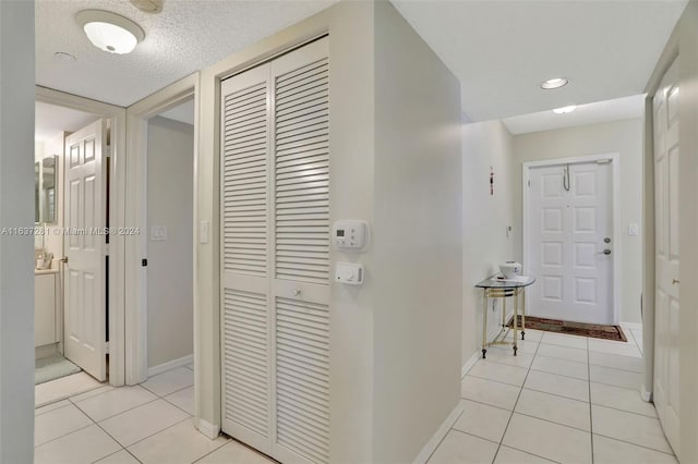 corridor with light tile patterned floors, a textured ceiling, recessed lighting, and baseboards