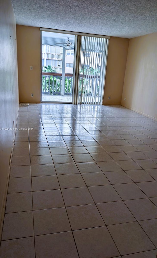 tiled empty room featuring ceiling fan, a textured ceiling, and a wall of windows