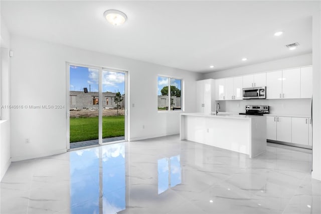 kitchen featuring stainless steel appliances, light tile patterned floors, white cabinets, a center island with sink, and sink