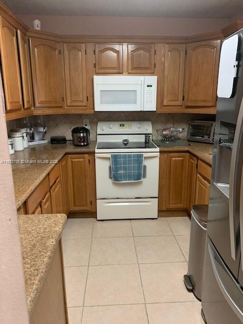 kitchen with tasteful backsplash, white appliances, light stone counters, and light tile patterned floors