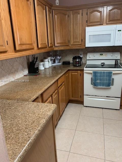 kitchen featuring tasteful backsplash, white appliances, light stone counters, and light tile patterned floors