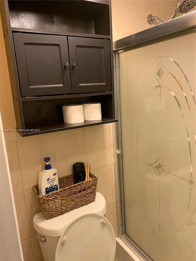 bathroom with tile walls, a shower with door, and toilet