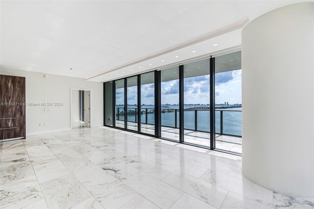 spare room featuring light tile patterned floors, a healthy amount of sunlight, a water view, and floor to ceiling windows