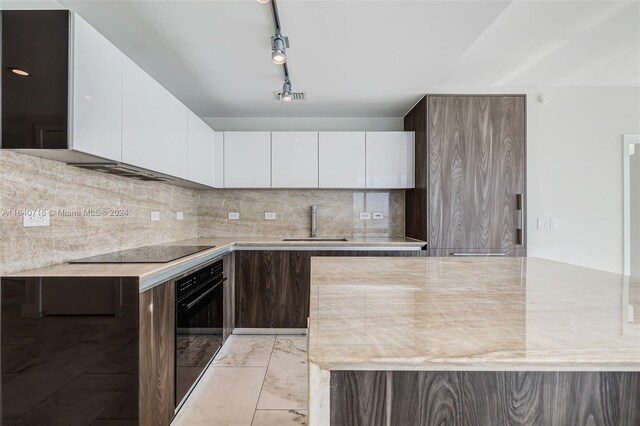 kitchen with light tile patterned floors, backsplash, track lighting, black appliances, and white cabinets