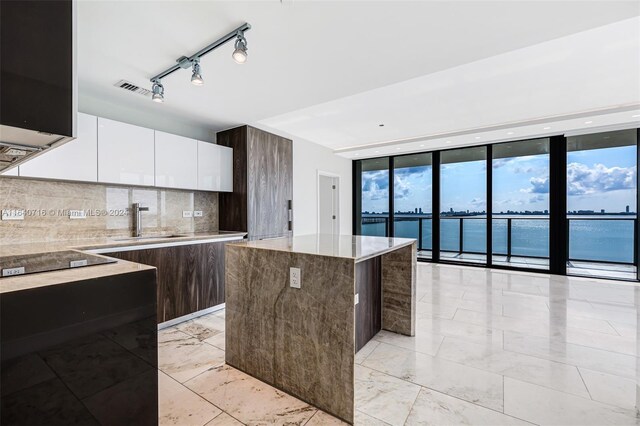 kitchen featuring decorative backsplash, white cabinets, track lighting, a kitchen island, and a water view