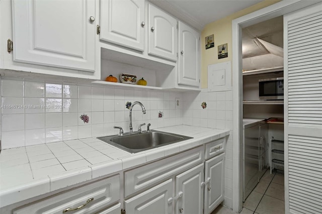 kitchen with tasteful backsplash, white cabinetry, stainless steel microwave, sink, and light tile patterned flooring