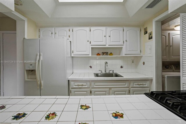 kitchen with decorative backsplash, sink, white cabinets, tile counters, and white refrigerator with ice dispenser