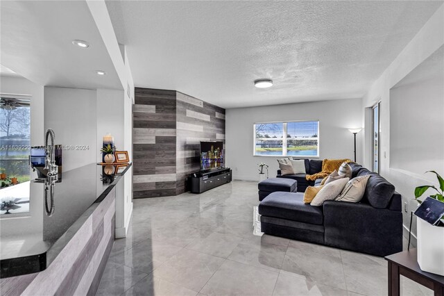 living room featuring tile walls, a textured ceiling, light tile patterned floors, and ceiling fan