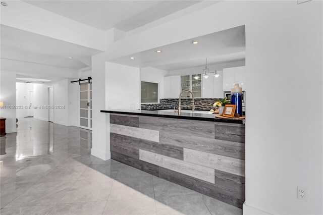 kitchen with decorative backsplash, white cabinets, a barn door, light tile patterned flooring, and sink