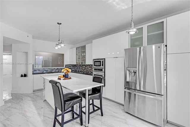 kitchen with stainless steel appliances, white cabinets, light tile patterned floors, a center island, and tasteful backsplash