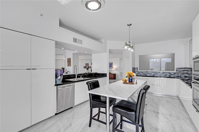 kitchen featuring dark countertops, marble finish floor, stainless steel appliances, white cabinetry, and a sink