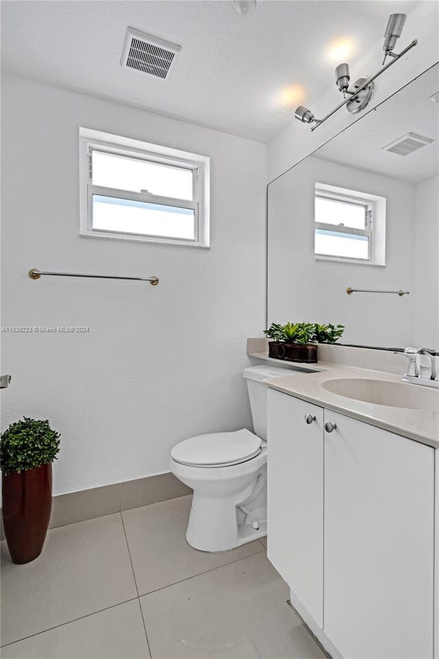 bathroom with tile patterned flooring, toilet, vanity, and a healthy amount of sunlight