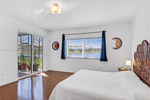 bedroom with access to outside, multiple windows, hardwood / wood-style floors, and a water view