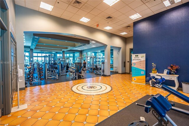 gym with a towering ceiling, light tile patterned flooring, and a paneled ceiling