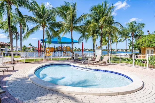 view of swimming pool featuring a water view, a patio area, fence, and playground community