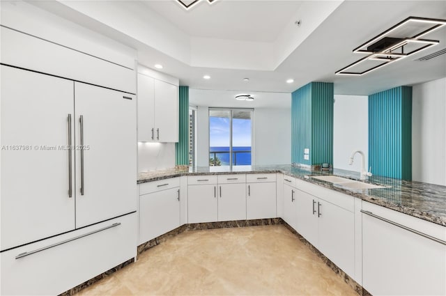 kitchen with white cabinets, paneled built in refrigerator, sink, and stone counters