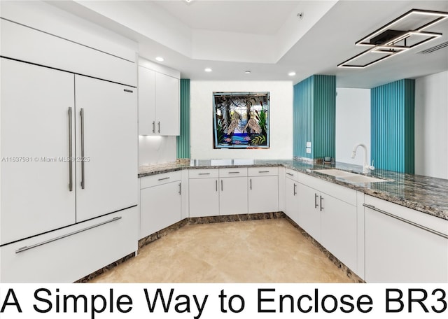 kitchen with sink, stone countertops, paneled refrigerator, a raised ceiling, and white cabinets