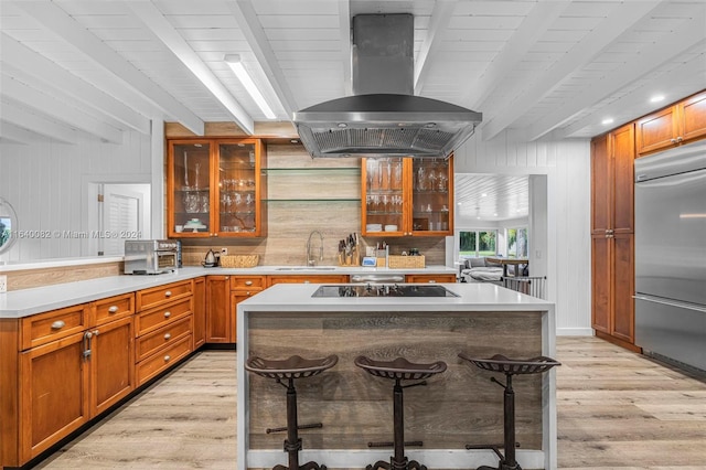 kitchen with a kitchen bar, stainless steel built in fridge, black electric stovetop, and island range hood