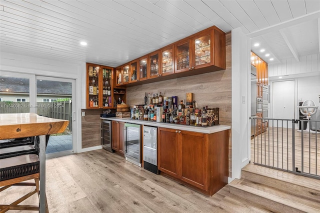 bar featuring light wood-type flooring, wood walls, and beverage cooler