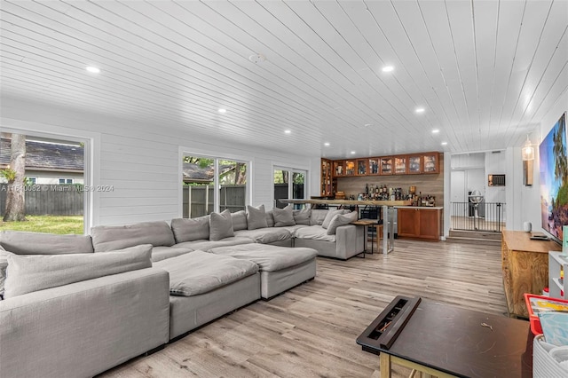 living room featuring light wood-type flooring, wooden walls, indoor bar, and wood ceiling