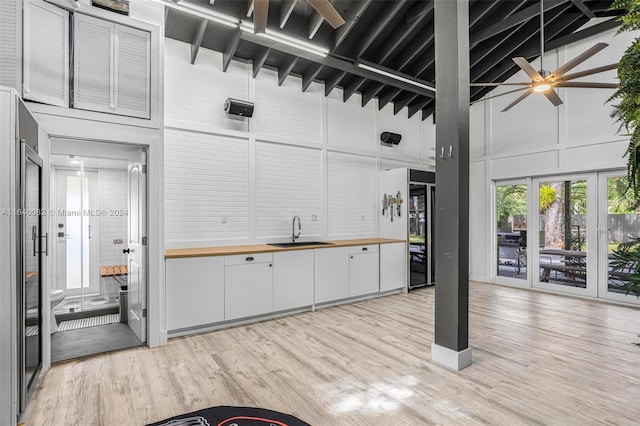 kitchen with wooden counters, white cabinets, sink, high vaulted ceiling, and light wood-type flooring