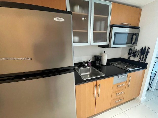 kitchen with light tile patterned floors, a sink, stainless steel appliances, glass insert cabinets, and dark countertops