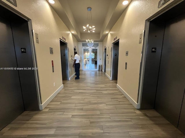 corridor with elevator, light wood finished floors, and an inviting chandelier