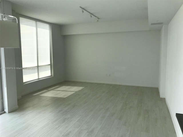 spare room featuring track lighting, plenty of natural light, and light wood-type flooring