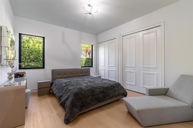 bedroom with light wood-type flooring, two closets, and a textured ceiling