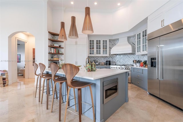 kitchen featuring custom range hood, built in appliances, light tile patterned flooring, tasteful backsplash, and white cabinetry