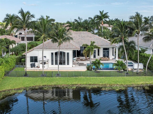 back of house with a fenced in pool, a lawn, a water view, and a patio area