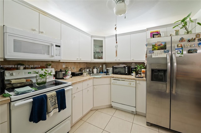 kitchen with white appliances, backsplash, light tile patterned floors, and white cabinets