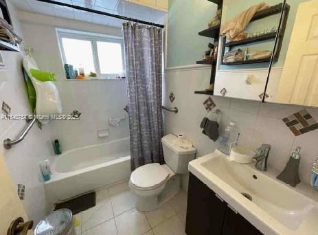 full bathroom with shower / tub combo, tile patterned flooring, tile walls, vanity, and toilet