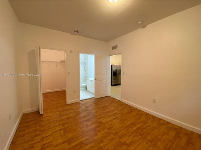 unfurnished bedroom featuring light hardwood / wood-style flooring, a walk in closet, a closet, and stainless steel refrigerator with ice dispenser