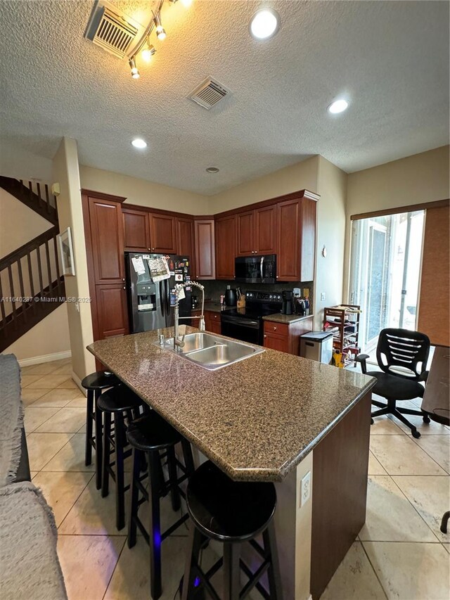 kitchen with a kitchen bar, sink, black electric range, stainless steel fridge with ice dispenser, and a kitchen island with sink