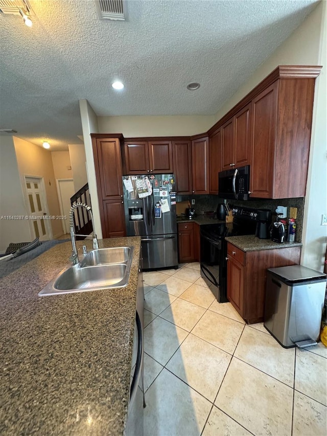 kitchen with sink, backsplash, light tile patterned floors, black appliances, and a textured ceiling