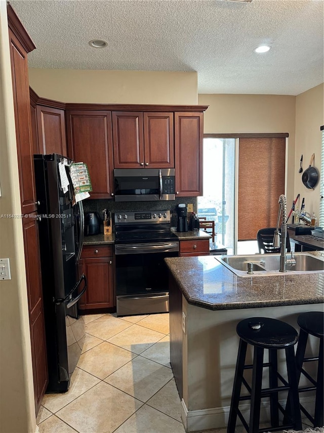 kitchen with sink, light tile patterned floors, stainless steel appliances, a kitchen breakfast bar, and a textured ceiling