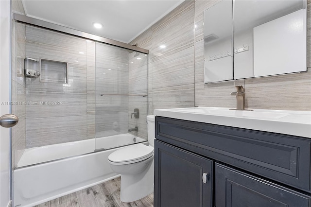 full bathroom featuring combined bath / shower with glass door, vanity, tile walls, hardwood / wood-style floors, and toilet