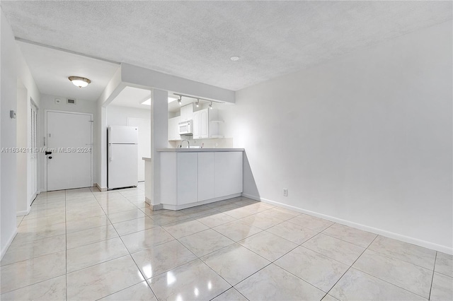 kitchen featuring white cabinetry, sink, white fridge, a textured ceiling, and light tile patterned floors