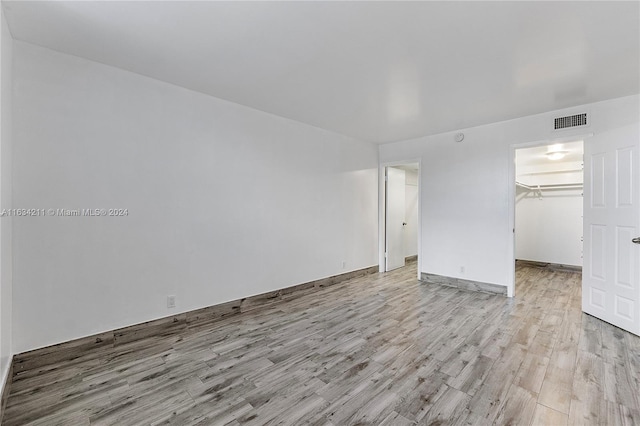 unfurnished bedroom featuring a spacious closet, a closet, and light wood-type flooring