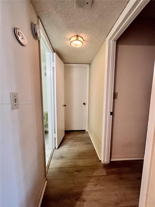 corridor with a textured ceiling and hardwood / wood-style floors