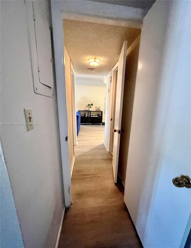 corridor with light wood-type flooring and a textured ceiling