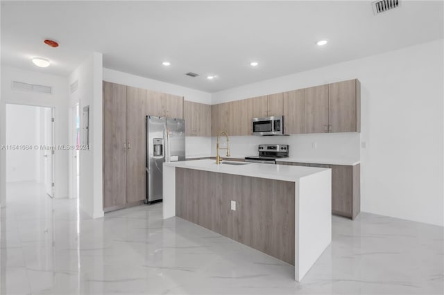 kitchen with appliances with stainless steel finishes, sink, light tile patterned floors, and a kitchen island with sink