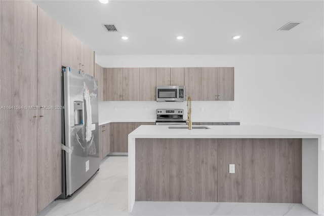 kitchen featuring light tile patterned floors, appliances with stainless steel finishes, an island with sink, sink, and light brown cabinets