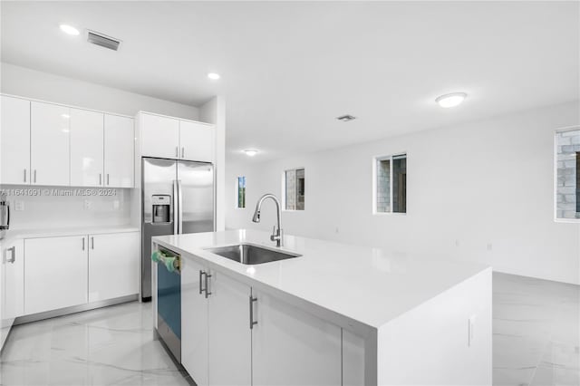 kitchen with white cabinets, sink, light tile patterned floors, and a center island with sink