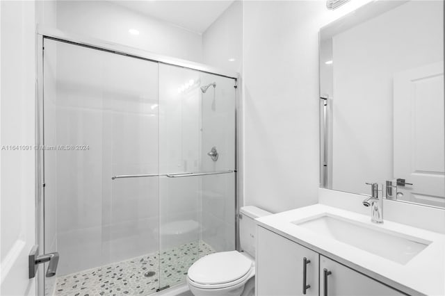 bathroom with a shower with shower door, vanity, and toilet