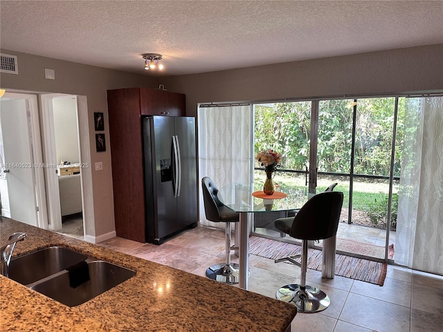 kitchen with dark stone countertops, stainless steel fridge with ice dispenser, sink, and a textured ceiling