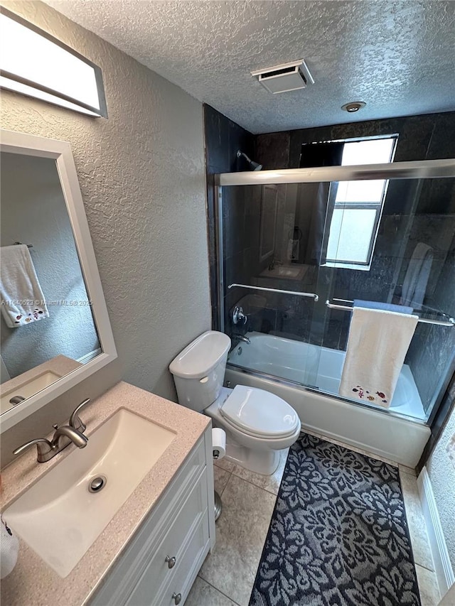 full bathroom featuring vanity, shower / bath combination with glass door, tile patterned flooring, toilet, and a textured ceiling