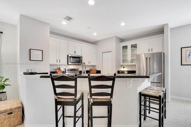 kitchen with dark stone counters, light tile patterned floors, stainless steel appliances, a breakfast bar area, and white cabinets